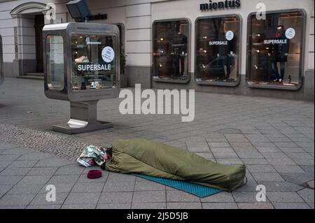 02/05/2022, Berlin, Deutschland, Europa - Ein Obdachloser schläft in seinem Schlafsack auf dem Bürgersteig vor einem Modehaus am Kurfürstendamm. [Automatisierte Übersetzung] Stockfoto