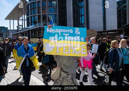 '16.04.2022, Berlin, Deutschland, Europa - Ukrainer und Anhänger protestieren während einer Demonstration unter dem Motto ''Marsch für den wahren Frieden in der Ukraine'' im Rahmen des alternativen Ostermarsches, der sich gegen die russische militärische Aggression in den beiden Kriegen in der Ukraine und in Syrien richtet. Ein Demonstrator hält ein Plakat mit der Aufschrift ''Waffen und Panzer für den Frieden'' ('Waffen und Panzer für den Frieden'') hoch. Die Demonstranten fordern weitere Sanktionen gegen Russland und mehr Unterstützung durch den Westen in Form von Verteidigungswaffen sowie einen sofortigen Boykott von Energieimporten aus Russland wie Öl und Gas. Stockfoto