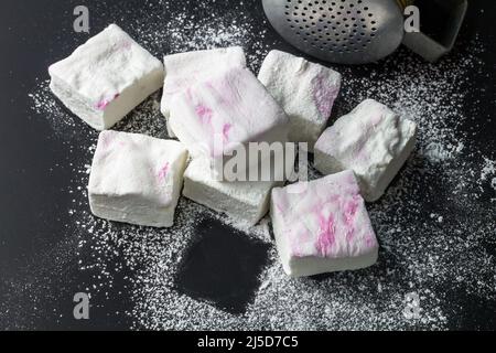 Hausgemachte rosa und weiße Sumpflaibe - Sumpflaibe mit Zucker auf schwarzem Hintergrund mit Kopierraum bestäubt Stockfoto