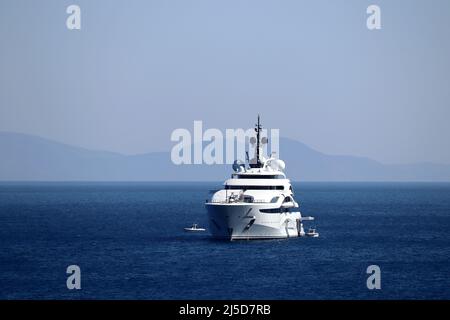 Luxusyacht mit Hubschrauberlandeplatz und Hubschraubersegeln im Meer, Vorderansicht. Weißes Boot im Hintergrund einer Berginsel Stockfoto