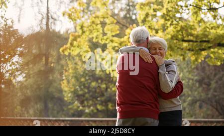 Europäisches älteres grauhaariges Rentnerpaar umarmte sich nach einem spontanen Tanz im Park. Herbststimmung. Hochwertige Fotos Stockfoto