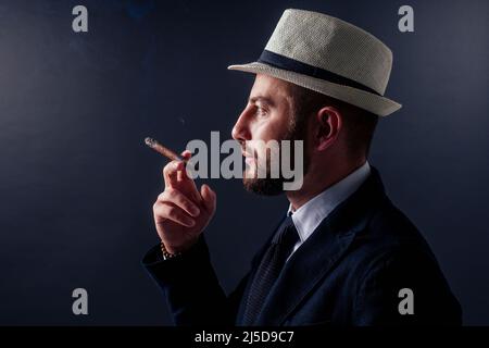 Porträt eines attraktiven Geschäftsmannes mit Zigarre im Studio mit schwarzem Hintergrund Stockfoto