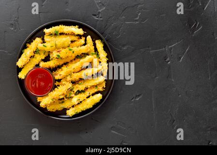 Gebratene Zucchini-Sticks auf Teller über dunklem Steinhintergrund mit Kopierraum. Draufsicht, flach liegend Stockfoto