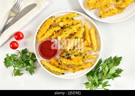 Knusprig gebratene Zucchini-Sticks und Tomatensauce auf dem Teller auf hellem Steingrund. Draufsicht, flach liegend Stockfoto