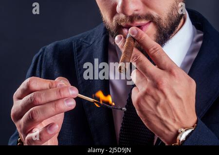 Porträt eines attraktiven Geschäftsmannes mit Zigarre im Studio mit schwarzem Hintergrund Stockfoto