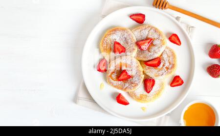 Hüttenkäse-Pfannkuchen mit Erdbeerscheiben auf weißem Hintergrund mit Kopierfläche. Draufsicht, flach liegend Stockfoto