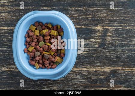 Katze getrocknetes Futter in einer blauen Plastikschale auf Holzhintergrund, Draufsicht, Nahaufnahme, Kopierraum Stockfoto
