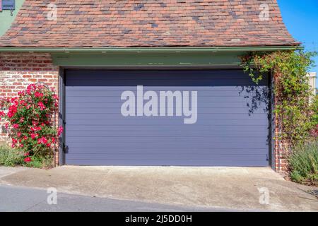 Außengarage mit verwitterten Ziegelwänden und purpurfarbenem, aufrolltem Holzgaragentor. Residenz in einem schrägen Gebiet in San Francisco, Kalifornien mit Schiefer g Stockfoto