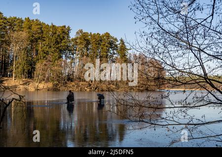 Weitwinkelaufnahmen von zwei Menschen, die auf einem teilweise gefrorenen See in polnischer Umgebung in der Nähe des Dorfes Drzewicz in der woiwodschaft Pommern fangen. C Stockfoto