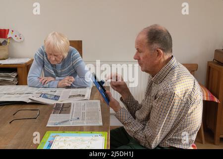 Ein älteres kaukasisches Paar las Zeitungen und überprüfte soziale Medien, während es an einem Esstisch saß, England, Großbritannien Stockfoto