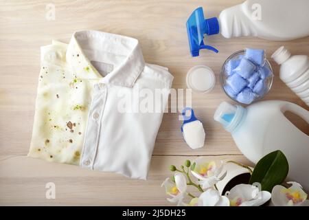 Vergleichendes Konzept des Waschens von Kleidung mit chemischen Produkten mit Hemd halb schmutzig halb sauber auf Holzbank mit verschiedenen Waschprodukten herum. T Stockfoto