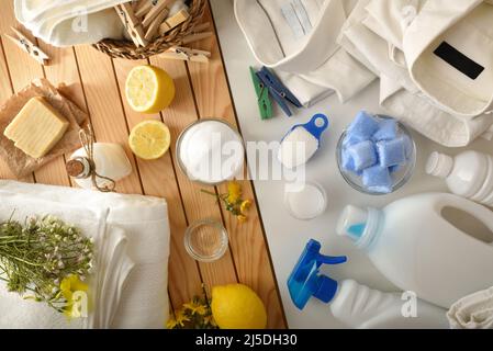 Vergleich von ökologischen Wäschereireinigungsprodukten auf Holztisch und Chemikalien auf weißem Tisch. Draufsicht. Horizontale Zusammensetzung. Stockfoto