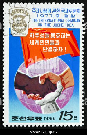 NORDKOREA - UM 1977: Eine in Nordkorea gedruckte Briefmarke zeigt verbundene Hände verschiedener Rassen, Banner und Globe, um 1977 Stockfoto