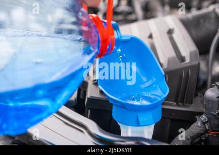 Nahaufnahme des Fahrers, der blaue, nicht gefrierende Scheibenwaschflüssigkeit in den Tank des Fahrzeugs gießt. Stockfoto