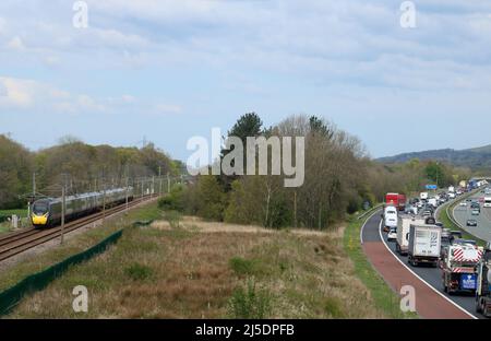 Mit dem Zug geht es schneller. Ein pendolino-Elektrozug fährt entlang der West Coast Main Line, während der Verkehr auf der angrenzenden M6 zu einem Kriechgang reduziert wird. Stockfoto