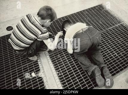 Zwei junge Jungen, die durch das Subway-Gitter auf dem Bürgersteig gucken, während sie eine Schnur mit einem Verschluss absenken, um einen Preis zu ergattern, New York City, New York, USA, Angelo Rizzuto, Anthony Angel Collection, Juni 1959 Stockfoto