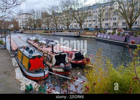 Narrowboote dockten an Little Venice, Regent’s Canal. Die Menschen gehen auf dem Treidelpfad und Regency weiß gestrichenen Stuckterrassen Stadthäuser im Hintergrund. London. Stockfoto