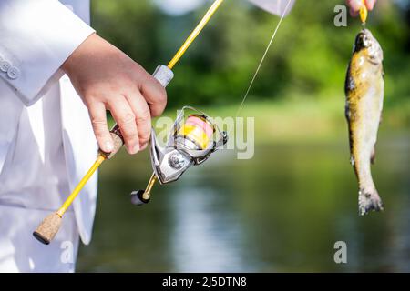 Der Mensch hält große Fischforellen in den Händen. Fischer und Trophäenforelle. Mann, der einen Forellenfisch hält. Angeln. Fischer Hand hält Angelrute mit Haspel Stockfoto