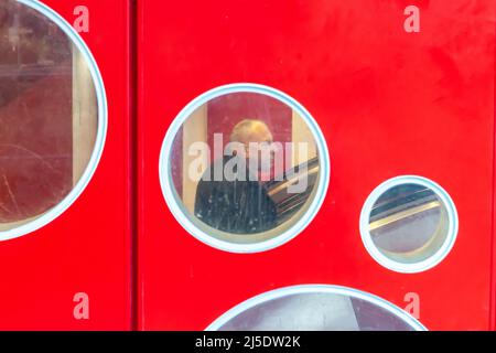 Mann auf einer Rolltreppe, gesehen durch eines der Bullaugen an einer roten Wand. Brüssel. Stockfoto