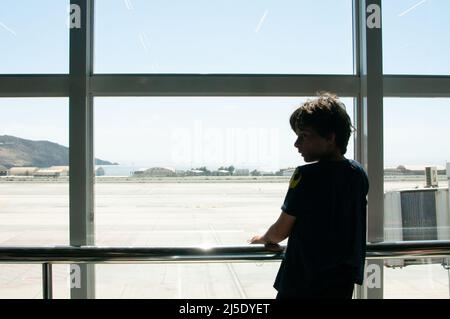 Junge, der aus dem Fenster zum Flughafen schaute Stockfoto