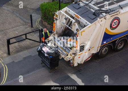 London, UK-17.04.22: Ein Mann, der Müllcontainer in einen Hecklader-Lkw in einer City of Westminster, im Zentrum von London, auslädt Stockfoto