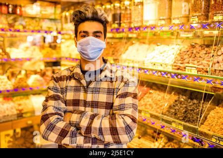 Schöner arabischer Mann trägt medizinische Maske Verkäufer Süßigkeiten in seinem Geschäft Basar Stockfoto