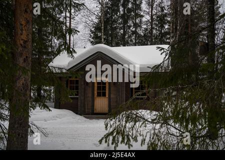 Rovaniemi, Finnland - 18.. März 2022: Eine Holzhütte in einem verschneiten Tannenwald an einem bewölkten Wintertag in Finnland. Stockfoto