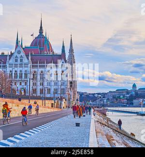 BUDAPEST, UNGARN - 20. FEBRUAR 2022: Genießen Sie den Spaziergang entlang der Donau mit Blick auf das Parlamentsgebäude und die Budaer Burg im Hintergrund, am 20. Februar in Stockfoto