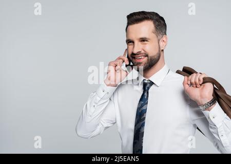 Fröhlicher Geschäftsmann im weißen Hemd ruft auf dem Smartphone und schaut isoliert auf grau weg Stockfoto