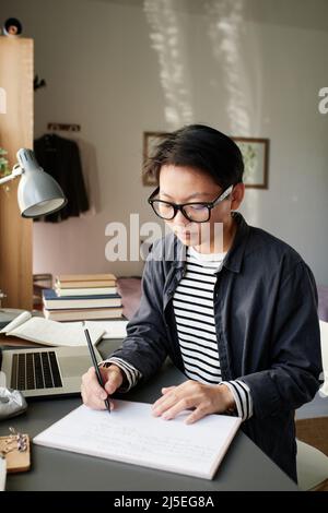 Seriöser junger asiatischer Mann mit Brille, der mit Laptop am Schreibtisch sitzt und den Wochenplan plant Stockfoto