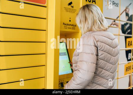 Poznan, Polen - 12. April 2022 Gelbes Shopping-Schließfach inPost mit Frau Eingabe Code, um es zu öffnen. E-Commerce-Versand und Lieferung Stockfoto