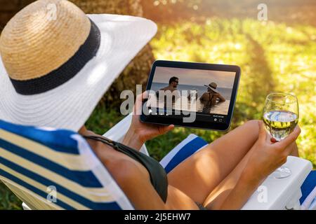 Frau, die einen romantischen Film über den Streaming-Media-Service ansieht, während sie sich im Gartenstuhl entspannt Stockfoto