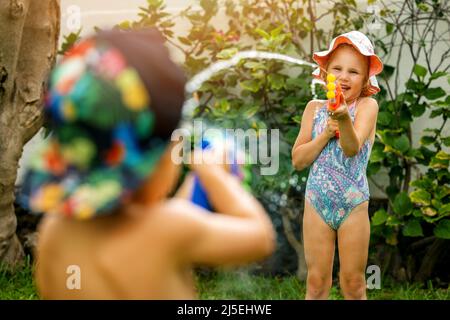 Kleine Mädchen und Jungen spielen mit Wasserpistolen im Garten am heißen Sommertag. Kinder Spaß im Freien Stockfoto