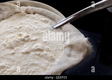 Trennen der Molke vom hausgemachten Joghurt mit einer Käseschachtel und einem Sieb in einer Schüssel Stockfoto