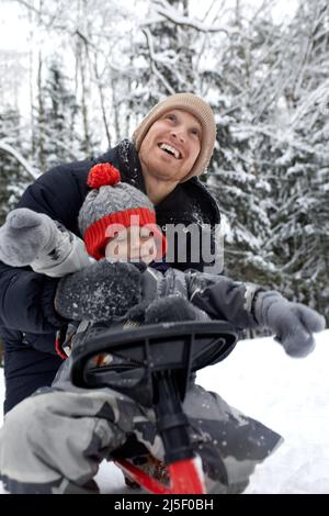 Vater und sein Sohn im lustigen Hut haben Spaß und lachen im verschneiten Winterwald. Fröhliche Familie in warmen Winterkleidung genießen Winterzeit im Schnee Stockfoto