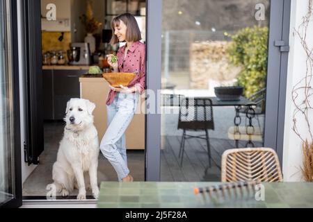 Frau steht mit ihrem entzückenden weißen Hund auf der Terrasse zu Hause zusammen Stockfoto