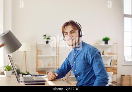 Glücklicher junger Mann, der Laptop und Kopfhörer verwendet und Online-Bildung genießt Stockfoto