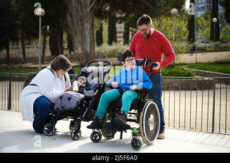Mutter und Vater genießen einen Familientag im Park mit ihrem Baby und einem behinderten Sohn im Rollstuhl. Stockfoto