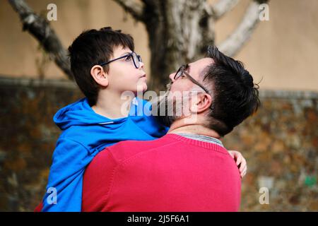 Mann hält und umarmt seinen behinderten Sohn, während sie Zeit zusammen im Freien genießen. Stockfoto