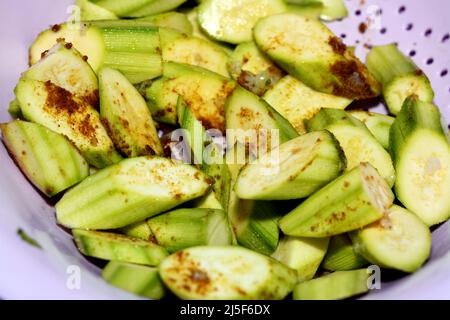 Frisch geschnittene Zucchinis in einer Plastikschüssel mit Gewürzen, roten Paprika, Salz und Kreuzkümmel, die mit Knoblauch und Öl, gesundem Essen, Gemüse und uns gegrillt werden können Stockfoto