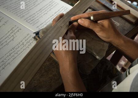 I Wayan Edi Wistara, ein balinesischer Praktiker von Palmblättern, schreibt alte balinesische Texte in seinem Haus in Karangasem, Bali, Indonesien, auf Palmblätter um. „Lontars wurden in den alten literarischen Texten geschrieben, die in der alten javanischen Sprache von Kawi und Sanskrit verfasst wurden. Die balinesische Schrift gilt als eine der komplexen Drehbücher aus Südostasien“, schrieb ein Team von Wissenschaftlern unter der Leitung von Made Windu Antara Kesiman (Laboratoire Informatique Image Interaction, Universität La Rochelle) während der Internationalen Konferenz über Grenzen in der Handschriftenerkennung 15. in Shenzen, China, 2016. Stockfoto