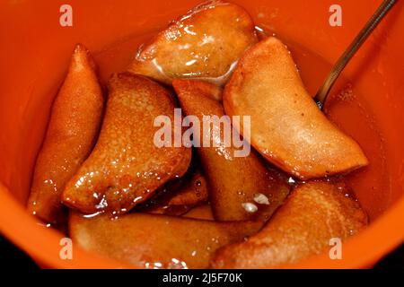 Eine Schüssel mit Qatayef-Knödeln gefüllt und gefüllt mit Nüssen und zerkleinerten Kokosnüssen, in tiefem Öl gebraten und mit Zuckersirup getränkt, arabischer Dessert gefaltet Pfanne Stockfoto