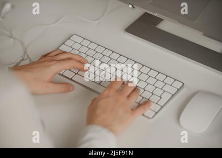 Nahaufnahme der Hände einer Frau, die auf einer kabellosen weißen Aluminium-Tastatur tippt. Stockfoto