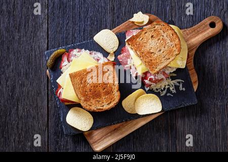 amerikanisches reuben-Sandwich mit Roggenbrot, dünn geschnittenes Corned Beef, Sauerkraut, russischem Dressing und geschmolzenem Käse an Bord mit Kartoffelchips, auf dunkel Stockfoto