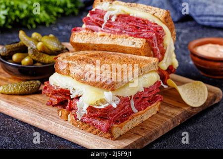 reuben Sandwich mit Roggenbrot in dünne Scheiben geschnittenes Corned Beef, Sauerkraut, russisches Dressing und geschmolzener Käse an Bord mit Gurken und Kartoffelchips, Clo Stockfoto