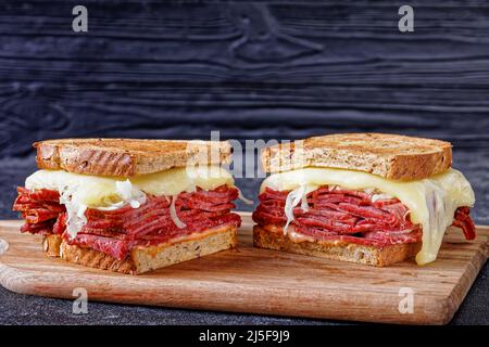 reuben-Sandwich mit Roggenbrot, dünn geschnittenem Corned Beef, Sauerkraut, Tausendinseln-Sauce und geschmolzenem Käse auf Holzbrett Stockfoto