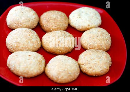 Arabisch-ägyptische orientalische Küche mit Datteln gefüllte Kekse und mit Sesam, Maamoul Eid El Fitr-Fest, Ramadan-Süßigkeiten und Desserts auf einer roten Plate bedeckt Stockfoto