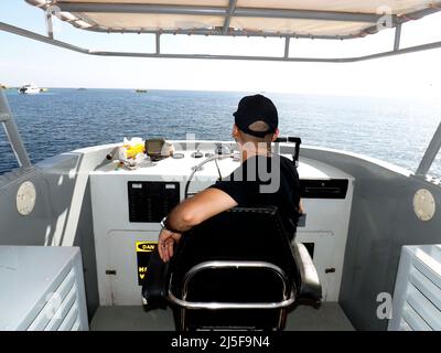 Sharm El-Sheikh, Ägypten, November 11 2014: Ein entspannter Kapitän auf einem Lenkrad und navigierende Segelboote oder Jachten, die im Roten Meer schwimmen, selektiv f Stockfoto