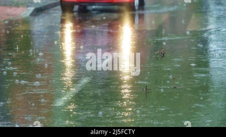 Regen fällt auf den Asphalt und Lichter im Auto erhellen die Szene. Stockfoto