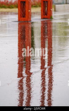 Starker Regen fällt auf den Boden und bildet Reflexionen mit Straßenmöbeln. Stockfoto